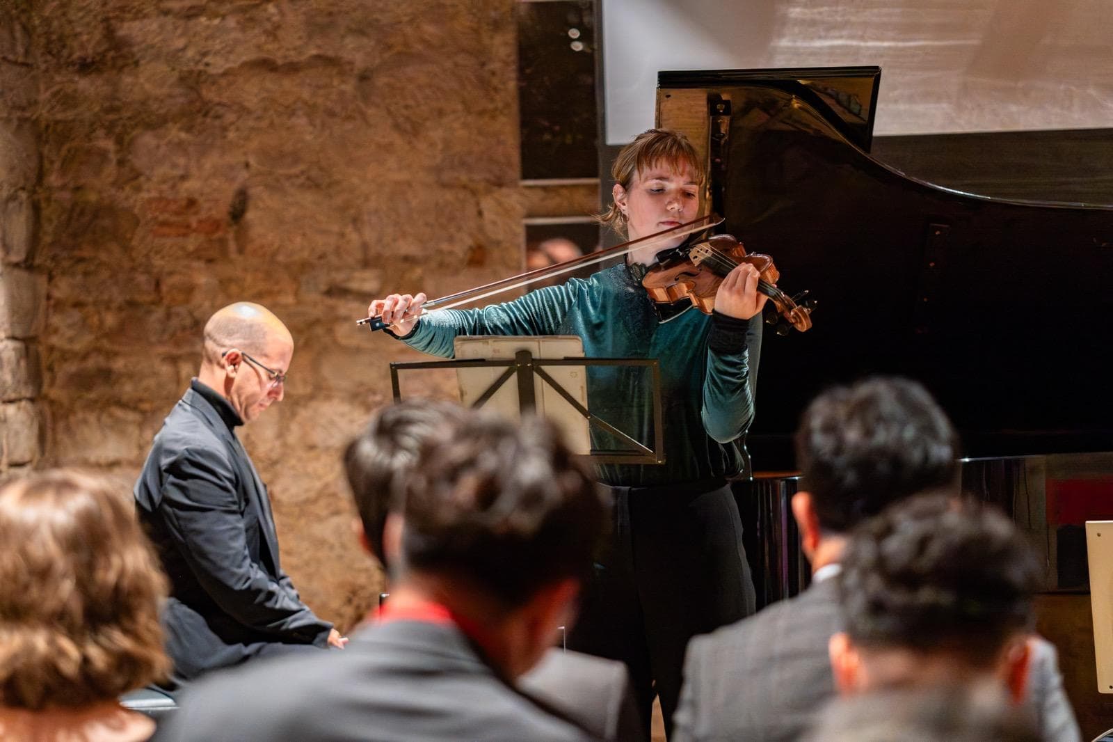 Annika Spegg spielt Geige in grünem Samt-Oberteil bei einem Kammerkonzert, links ein Pianist am Flügel.