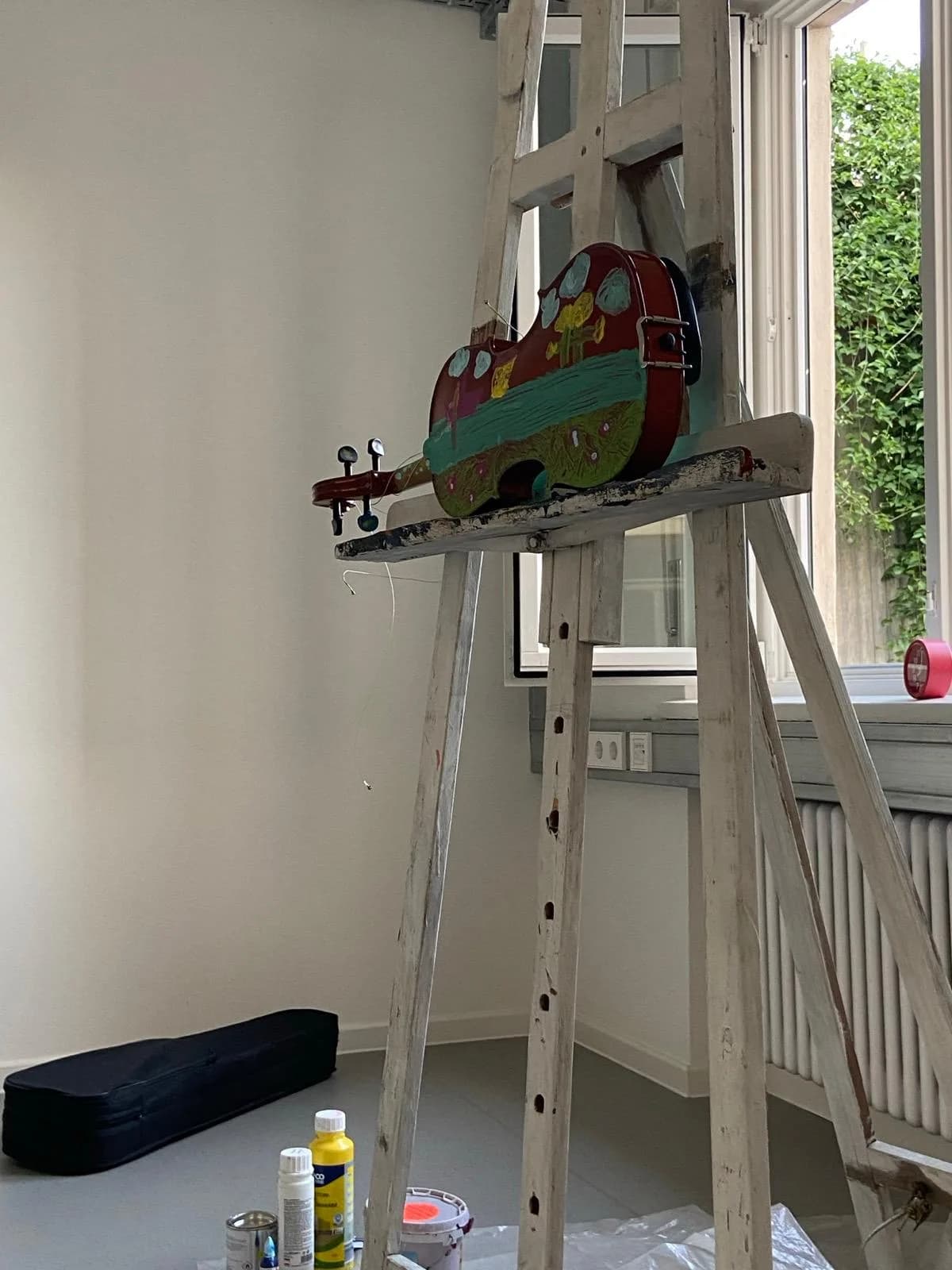 Bunt bemalte Geige auf einer Holzstaffelei in einem hellen Atelierraum.