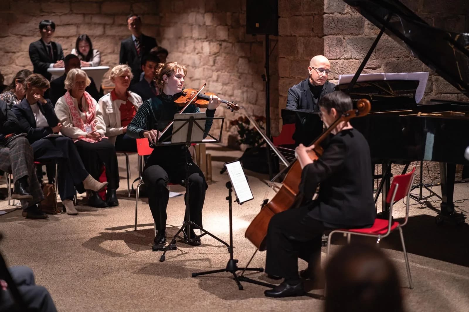 Annika Spegg im Trio mit Cellist und Pianistin in einem Konzertsaal mit Backsteinwand.
